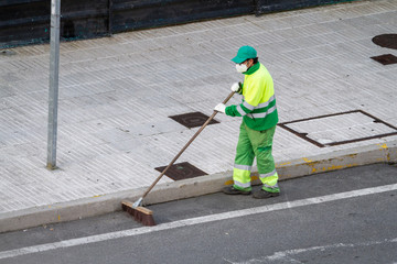 Street sweeper wearing face mask working on a sidewalk. Public cleaning concept during coronavirus pandemic