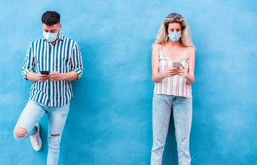 Young people using mobile phones while keeping social distance and wearing face medical mask - Friends watching video and texting with smartphone during coronavirus outbreak - Main focus on girl hands
