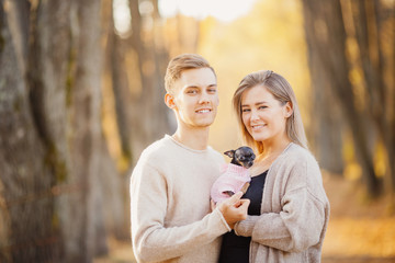 Loving couple cuddles in warm bright sweaters holding dwarf dog in their hands. Childfree Concept