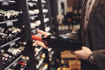 Fototapeta premium Bartender sommelier takes bottle of red wine from counter of restaurant drinks store