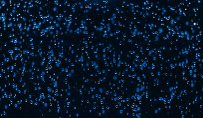 Falling blue drops of water on a black background. Rain. Macro photo of water..