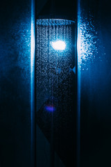 Drops of water fall from a watering can in the shower in blue light. Water drops close-up. Flow of water. A large round watering can in the shower..