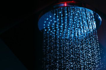 Obraz na płótnie Canvas Drops of water fall from a watering can in the shower in blue light. Water drops close-up. Flow of water. Big round watering can macro photo..