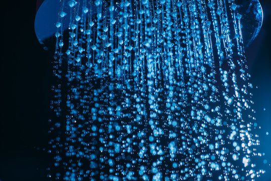 Drops of water fall from a watering can in the shower in blue light. Water drops close-up. Flow of water. Big round watering can macro photo..