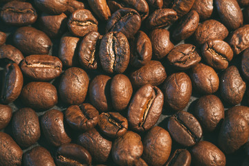 A scattering of coffee beans on a black countertop. The texture of the beans closeup. Vintage style photography..
