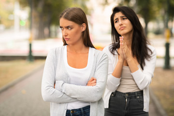 Girl Begging Offended Female Friend To Remain Friends Standing Outdoors