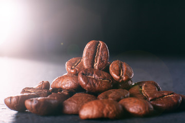 Grains of black coffee on a black granite countertop with yellow light from behind. Advertising photo of coffee. Photo with a glare from the light. Back light on a pyramid with grains..