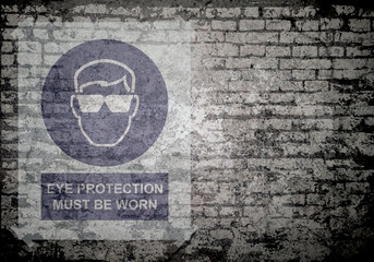 Grunge decayed faded brick wall background with eye protection must be worn sign with copy space for own text  