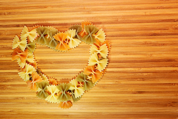 A heart made of multi-colored pasta on a wooden bamboo board.