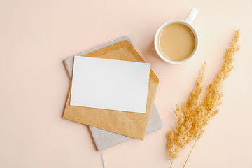 Fototapeta na wymiar Flat lay composition with envelope, invitation card mockup, cup of coffee and dry flowers on beige background. Top view wedding invitation or love letter
