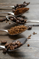 different textures of coffee in spoons on a wooden background, coffee beans, instant coffee, ground coffee