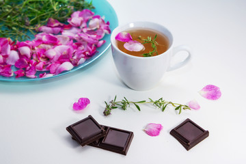 Homemade herbal tea in a white cup and chocolate pieces on the table. Tea rose petals and thyme on a plate - ingredients for hot healthy drink 