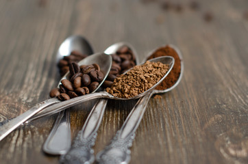 different textures of coffee in spoons on a wooden background, coffee beans, instant coffee, ground coffee