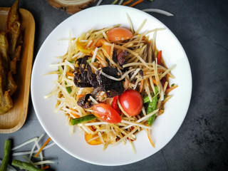 Thai Papaya Salad with Salted Crab and Fermented Fish with Fried wings chicken on dark background. Thai papaya salad or what we call 