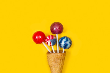 Piruletas de colores dentro de un cono de oblea de helado sobre un fondo amarillo brillante liso y aislado. Vista superior y de cerca. Copy space - obrazy, fototapety, plakaty