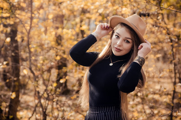 A beautiful young girl in a brown hat, black jacket and trousers walks in the park. Brown author's...