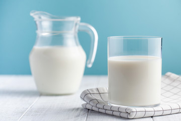  Glass and jug of milk on a blue background. The concept of farm dairy products, the use of milk, milk day. Copy space.