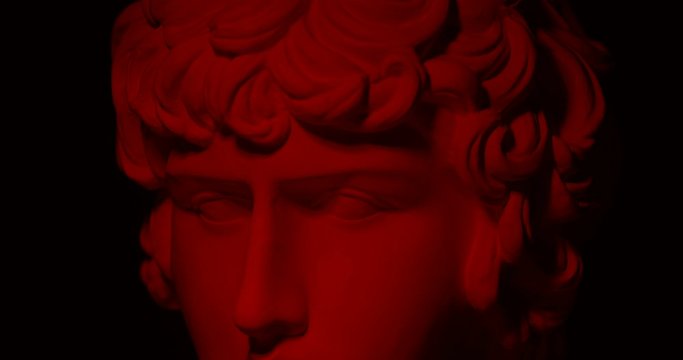 Epic studio close-up  shot of a gypsum head with moving and changing red lighting. The play of light and shadow on half the face of  statue of a man. On a black background isolated 4k
