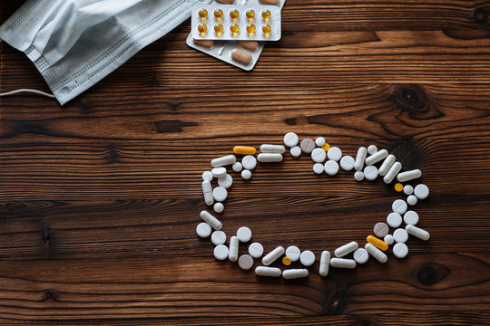 A variety of pills, tablets in a bister and medical mask on a wooden background
