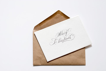 Greeting card with the inscription Merry Christmas on a brown craft envelope on a white background.