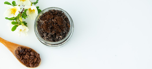 Body scrub made from ground coffee and sugar on a white background, homemade cosmetic product for peeling and spa care. Coffee beans in a wooden spoon and a flowering branch. Top view.