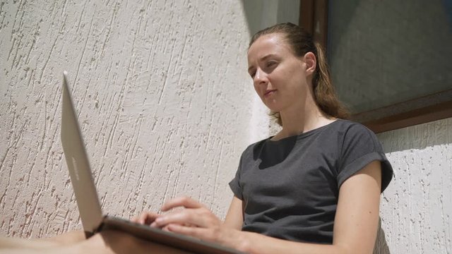 Beautiful young woman working from home on balcony on laptop