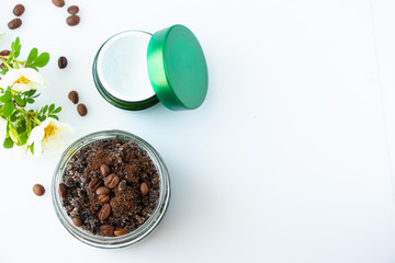 Body scrub made from coffee and sugar in a glass jar and face cream on a white background. The concept of home spa care and beauty. Flat lay top view.