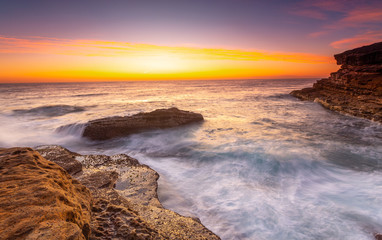 Sunrise over the ccean with some foreground rocks of eroded sandstone