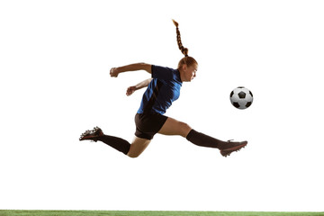 Fototapeta premium Young female soccer or football player with long hair kicking ball for the goal in flight, jumping high on white studio background. Concept of healthy lifestyle, professional sport, motion, movement.