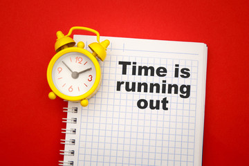 Time is Running Out - phrase on notebook with yellow alarm clock aside on red background.