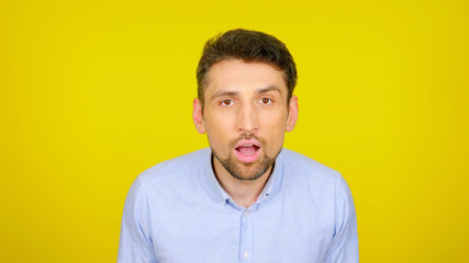 Surprised man in a light blue shirt on a yellow background with copyspace. The bearded guy is shocked by what he saw