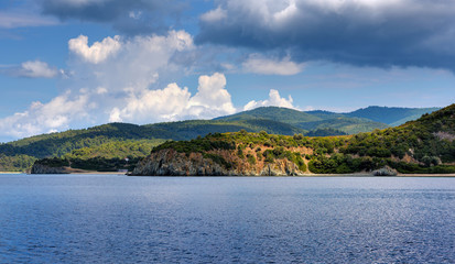 Obraz premium View of the shore from the sea. Landscape with the sea and beautiful clouds in the blue sky. Sithonia, Halkidiki, Greece.