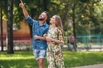 Fototapeta premium Beautiful young couple in love walking in the summer park with cold lemonade. Romantic couple on a date in the fresh air