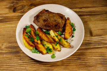 Fried beef steak with potato wedges on wooden table