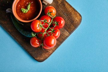 top view of delicious tomato sauce in bowl on wooden board with fresh ripe vegetables on blue background