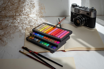 art pastel pencils on a table with brushes and a vintage camera