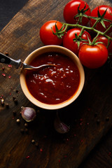 top view of delicious tomato sauce in bowl with spoon near tomatoes and spices on wooden board