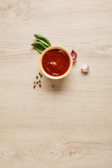 top view of delicious tomato sauce in bowl near spices on wooden table