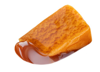 Caramel isolated on white background. Caramel piece with flowing toffee sauce, top view. Macro