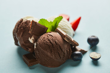 Selective focus of tasty brown and white ice cream with berries, chocolate and mint on blue background