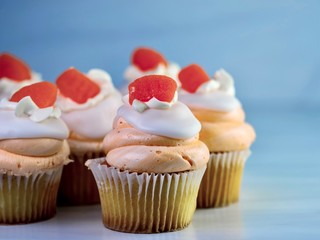 Yellow cupcakes with orange and white swirled frosting piled high and an orange gum drop candy on top.  Orange creamsicle cupcake, delicious baked goods.