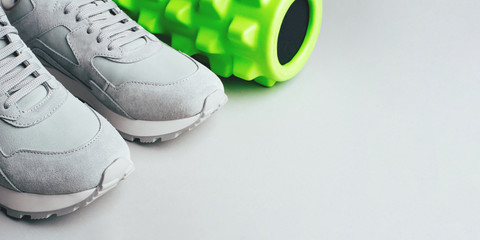 Grey sneakers and a massage roller on a gray background. Copy space for text.