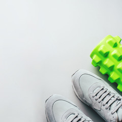 Grey sneakers and a massage roller on a gray background. Top view, copy space for text.