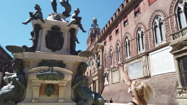 Lifestyle woman with the surgical mask in Maggiore square looking at Neptune statue and San Petronio basilica. Coronavirus after COVID-19 lockdown with social distancing in Bologna city of Italy.