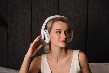 attractive woman touching wireless headphones while looking away