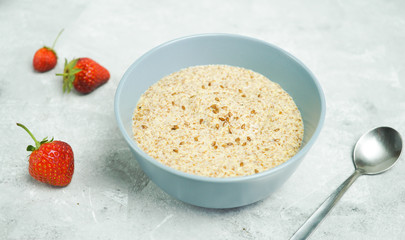 Flax porridge with strawberries in a bowl on a light background and copy space.