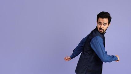 Scared Indian man running away from something on lilac background, copy space. Panorama