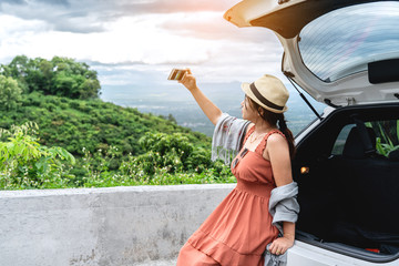 Happy and relaxation time in holiday Road Trip, Young woman traveler sitting on back car, Taking selfie photo and looking at beautiful mountain view with nature, Traveler car concept