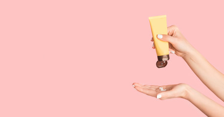 Closeup of young female applying hand cream on pink background, copy space. Panorama
