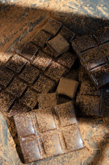 pieces of dark chocolate sprinkled with cocoa powder on a dark background